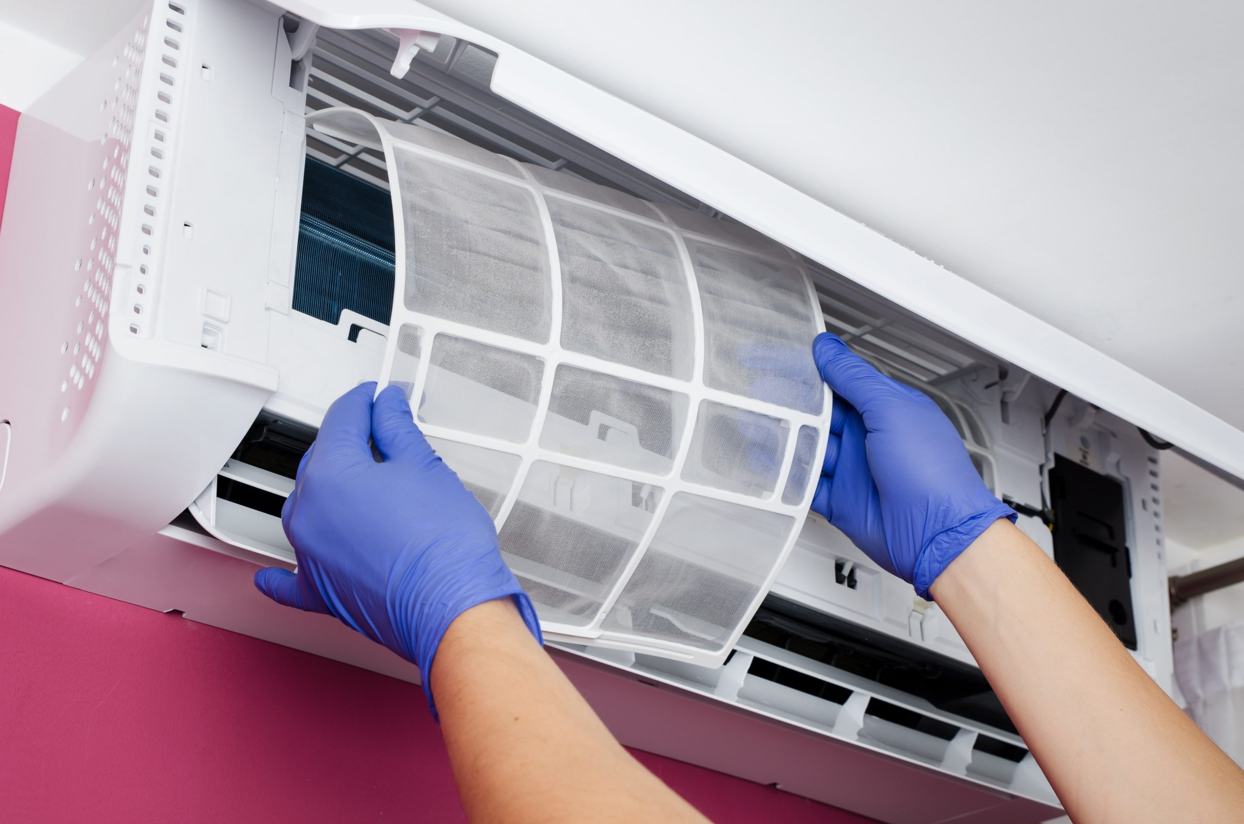 arms with blue gloves removing an air conditioning filter from a split system air conditioner