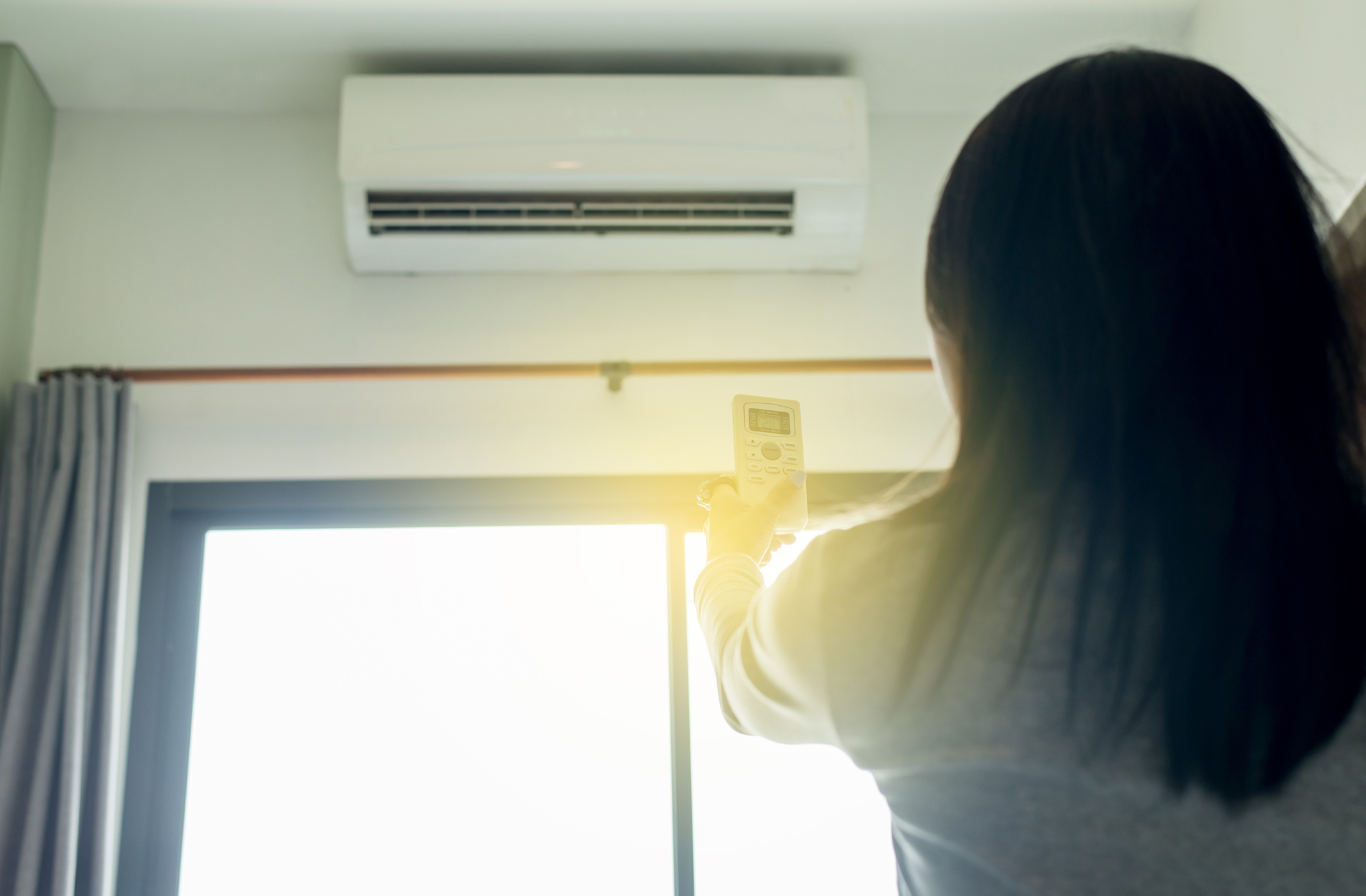 woman pointing remote control at split system air conditioner to enable dry mode